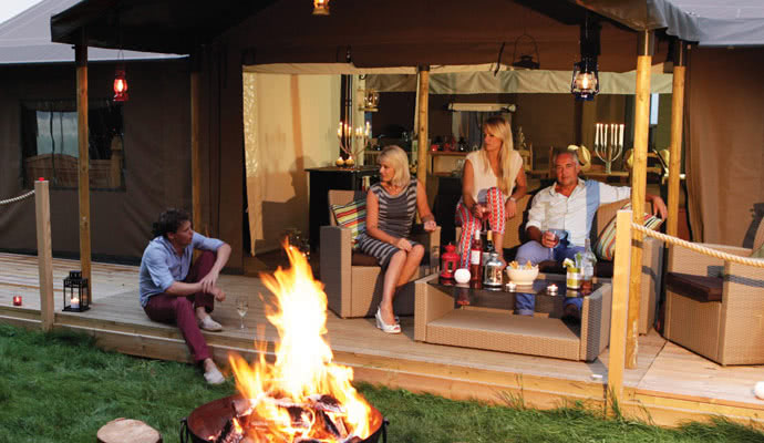 A family group realxing by thw fire pit of their glamping tent